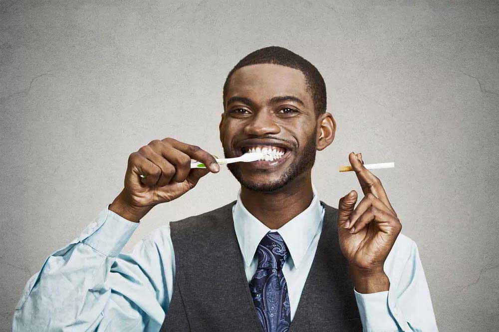 A man brushing teeth and holding cigrette