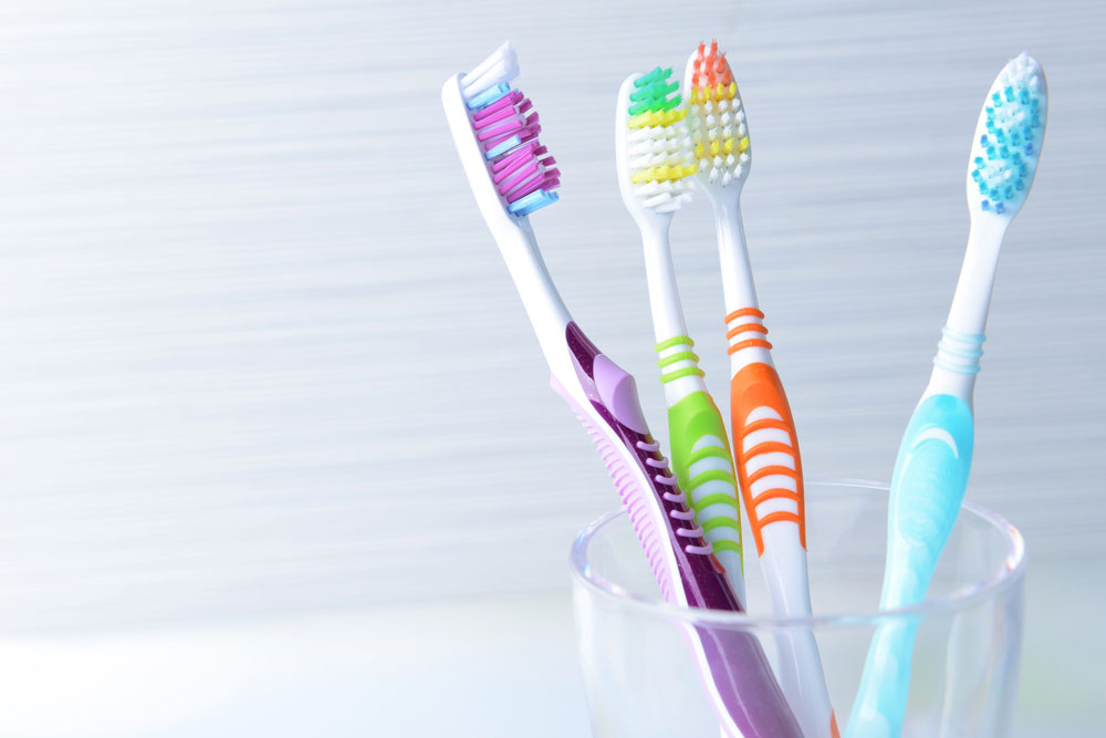 Three toothbrushes stored in a glass on a plain white surface