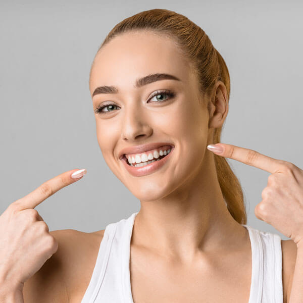 young happy woman with beaming smile, pointing to her teeth with both hands
