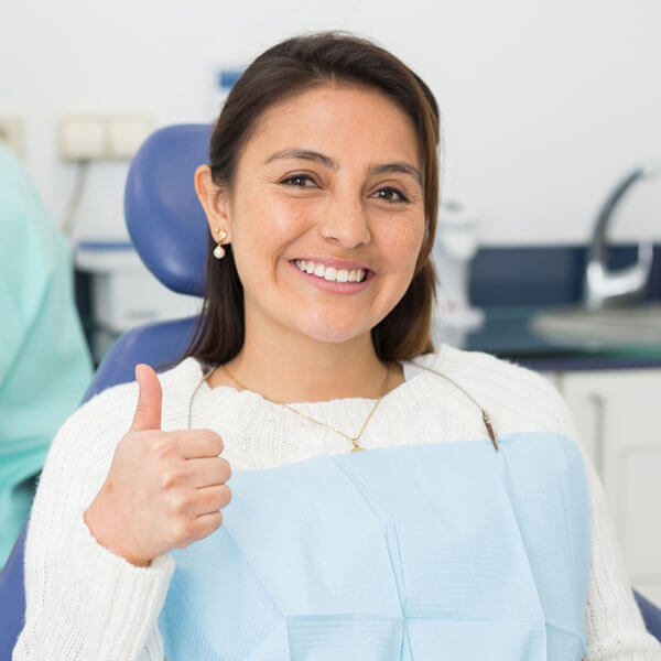 happy woman in dental chair smiling and giving the thumbs up